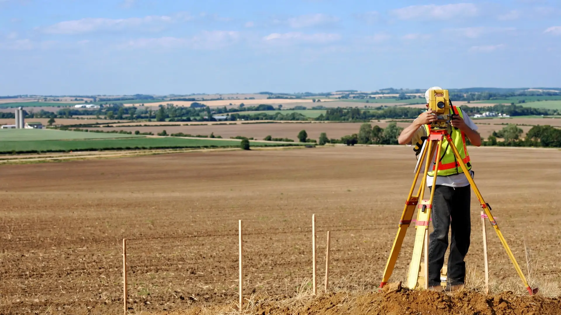 Técnico con una estación topográfica en una llanura agrícola